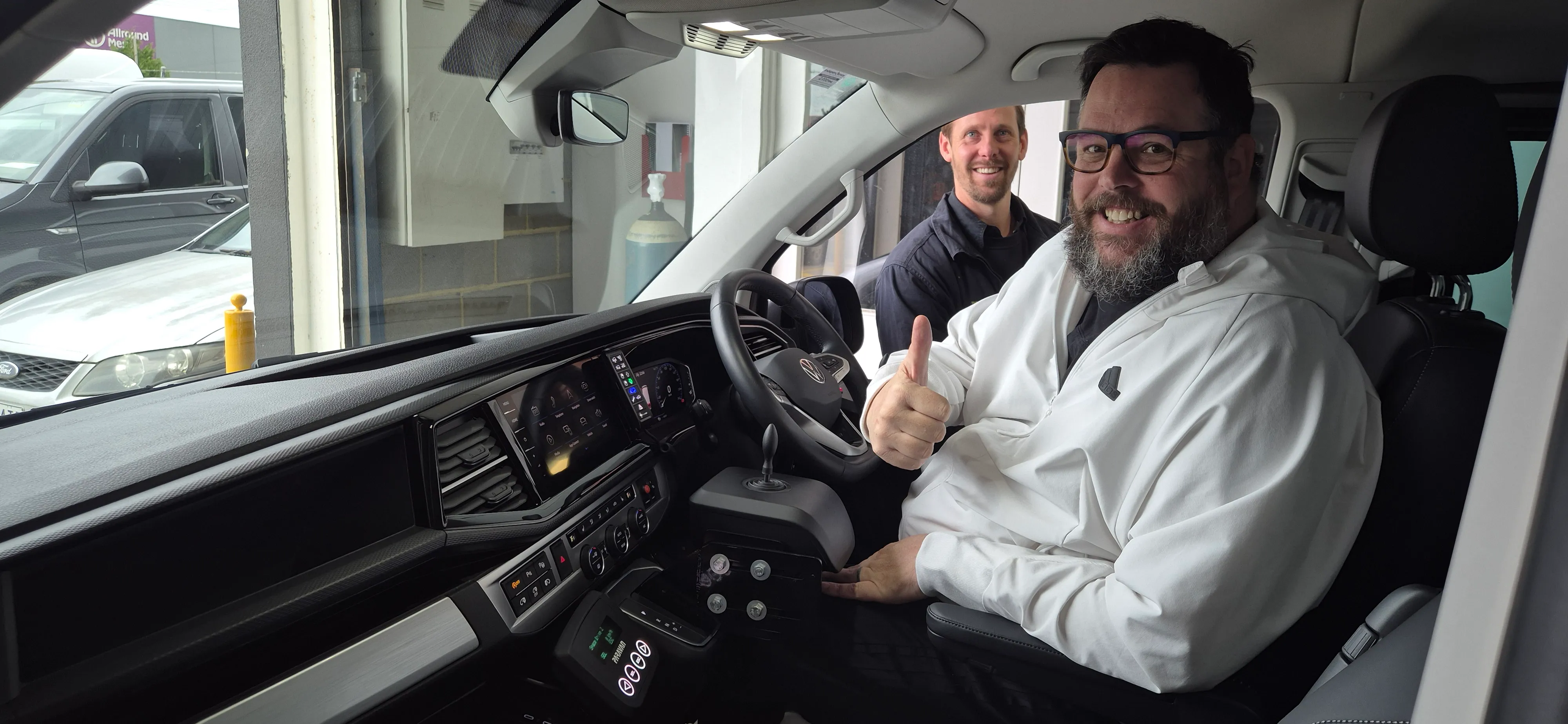 Two smiling men in a modified vehicle, one giving a thumbs up from the driver's seat